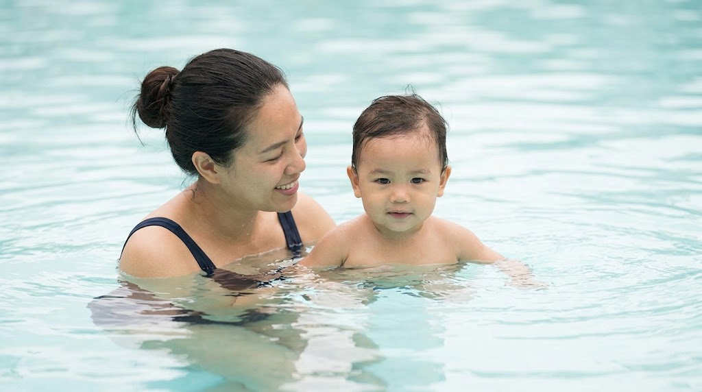 A parent smiles at a child submerged to the chest in clear pool water.
