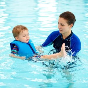 A child in a swim vest kicks water during a lesson with an instructor.