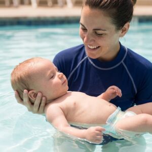 A smiling swim instructor gently supports a baby in the water, providing one-on-one guidance during a lesson.