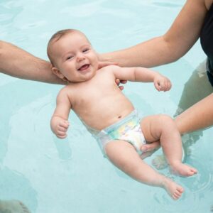 An infant with a swim diaper is happily supported while floating in a pool.